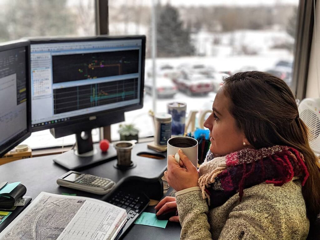 A woman sitting at a desk with two monitors and a cup of coffee at Muller Engineering Company in Lakewood, Colorado.