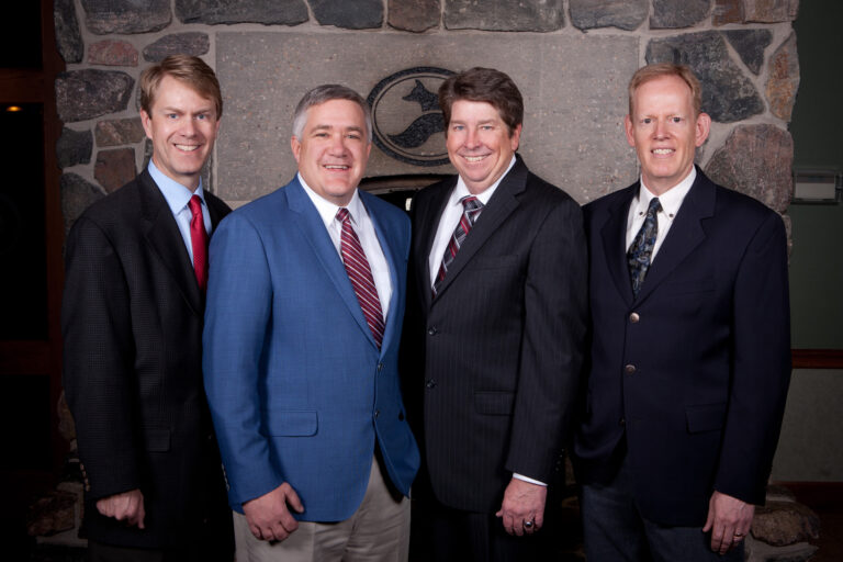 Four men in suits from Muller Engineering Company posing for a picture in front of a fireplace.