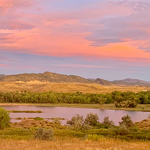 A pink sunset over Chatfield Reservoir and mountains.